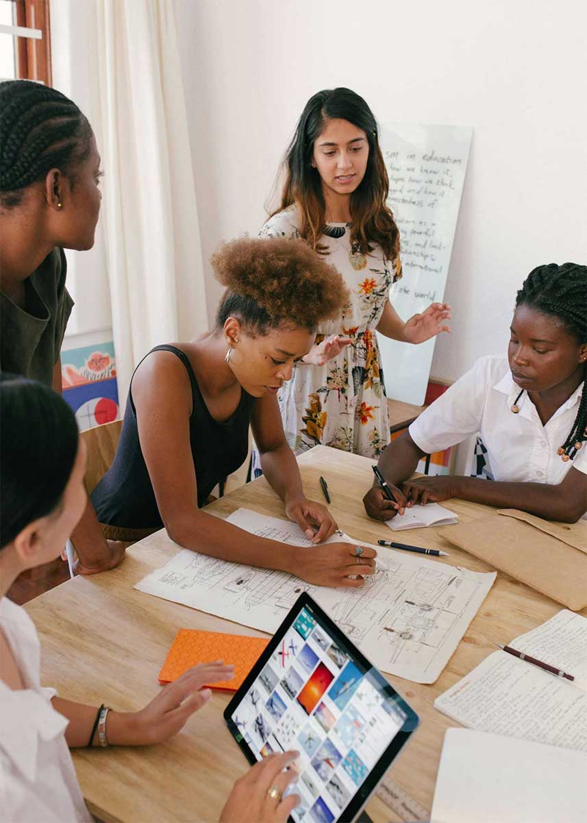 Illustrative photo: a team of employees or interns collaborate on a design project at a table with paper, whiteboards, and touchscreens