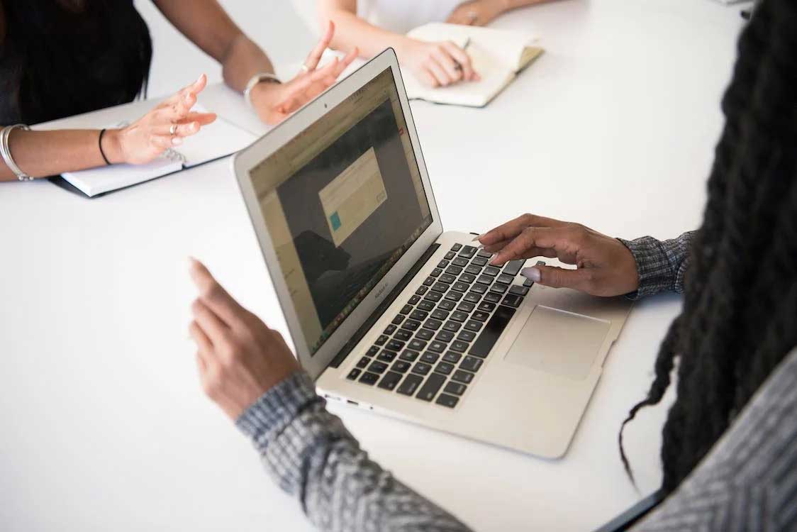 Illustrative photo: three people in a meeting across a desk, one with a laptop open