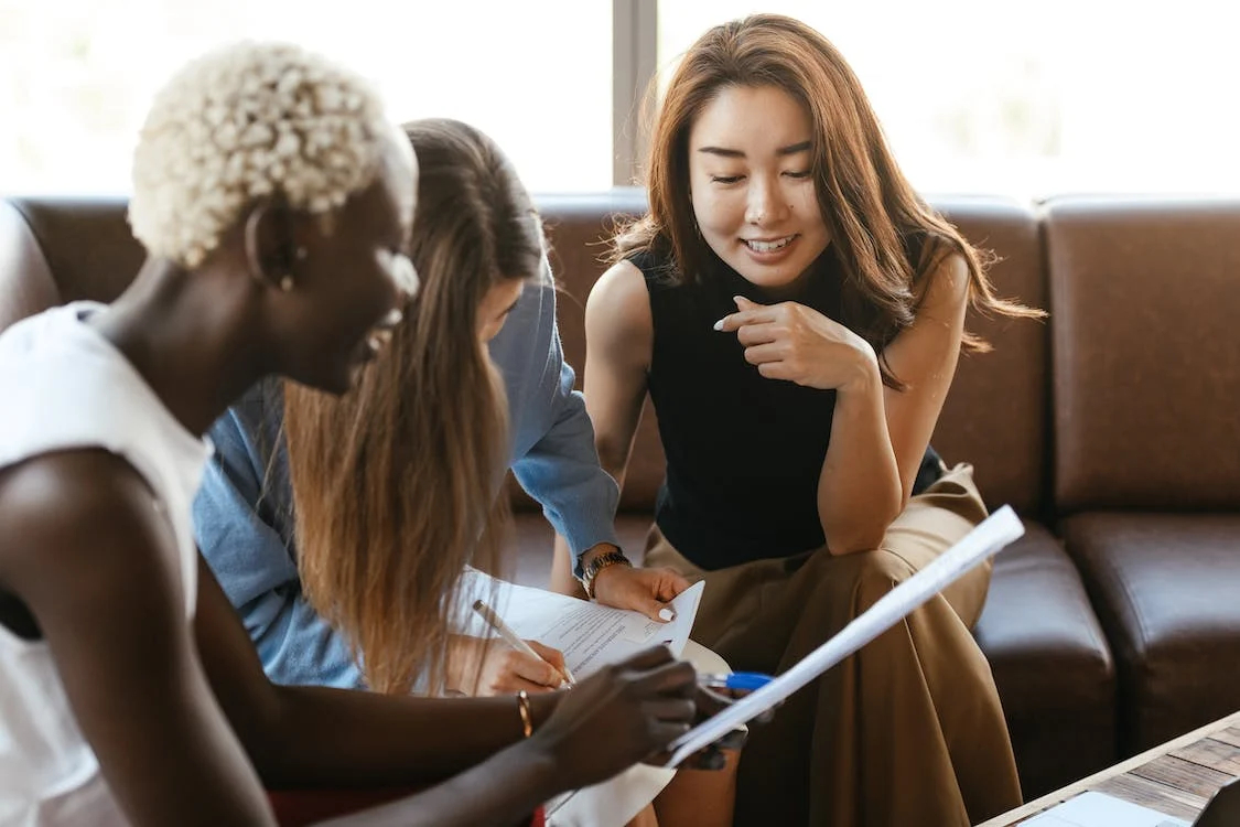 Illustrative photo: three people sit on an office sofa leaning in to discuss some papers with each other.